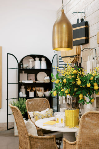 Gold pendant light with a white marble table and rattan chairs next to a wooden shiplap wall. Table filled with bright yellow garden spring decor. 