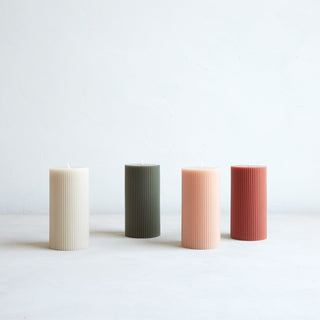 Ribbed pillar candles in white, green, pale pink, and salmon pink on white background.