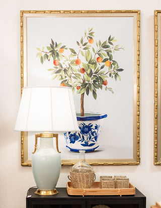 Thin gold lamp with white circular lampshade in an antique style. Sitting on couch table that is against a cream colored couch.