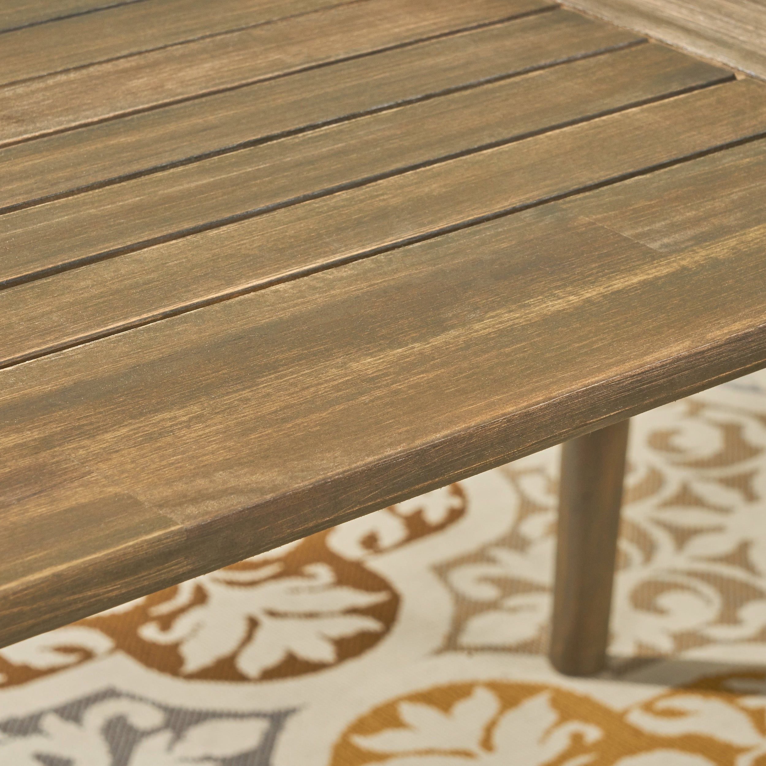 Close up of grey wooden outdoor dining table with tapered legs and woven rope detail at the top of legs.