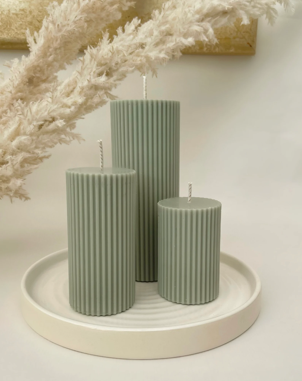 Two green ribbed pillar candles on whitewashed wooden bookshelf featuring other decor pieces.